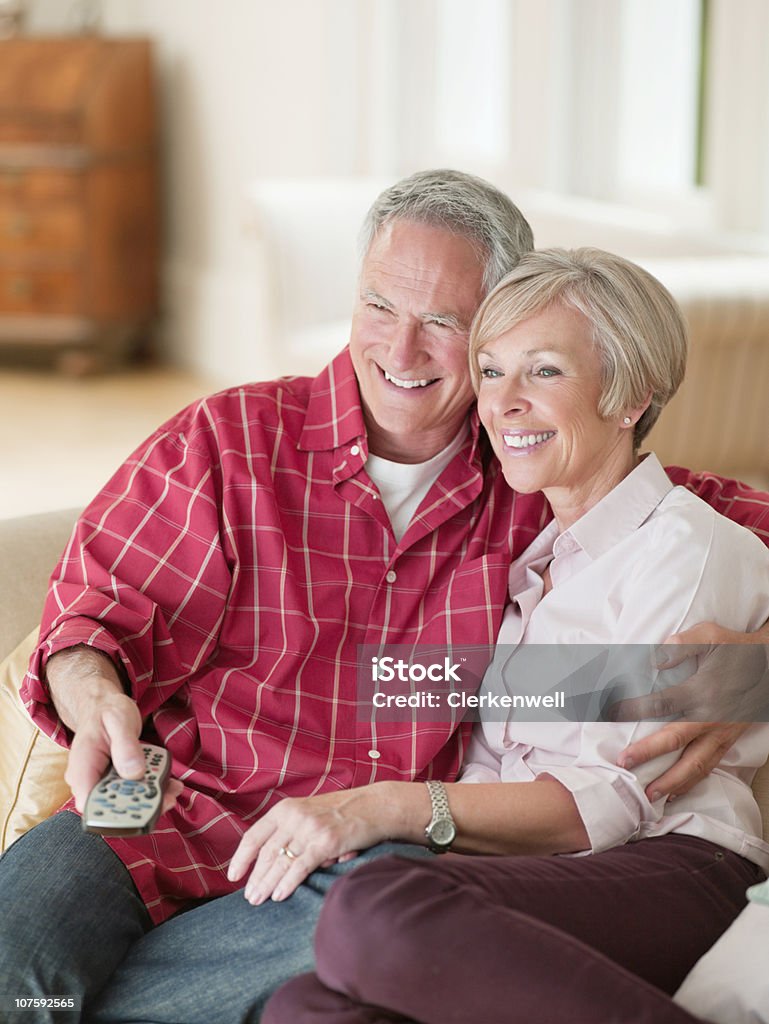 Joyeux couple assis ensemble sur le canapé avec une télécommande dans - Photo de 55-59 ans libre de droits