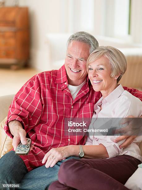 Photo libre de droit de Joyeux Couple Assis Ensemble Sur Le Canapé Avec Une Télécommande Dans banque d'images et plus d'images libres de droit de 55-59 ans