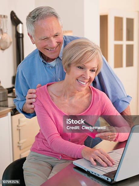 Pareja De Compras En Línea En Portátil En La Cocina Foto de stock y más banco de imágenes de 55-59 años