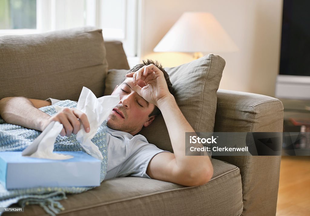 Homem com um resfriado deitado no sofá com lenços de papel - Foto de stock de Resfriado e Gripe royalty-free