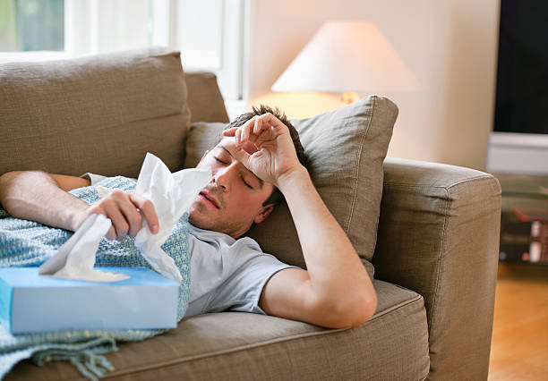 man with a cold lying in sofa holding tissues - snuva man bildbanksfoton och bilder