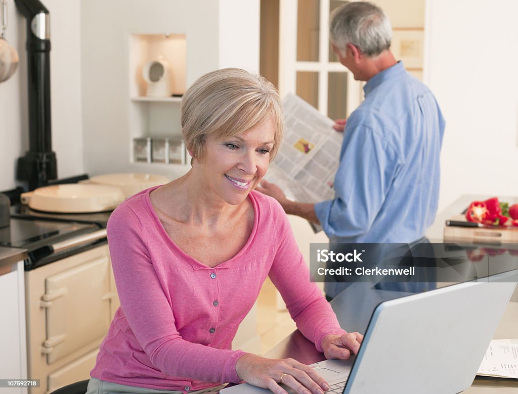 Mujer madura trabajando en la computadora portátil con el hombre mayor en el fondo - Foto de stock de Internet libre de derechos