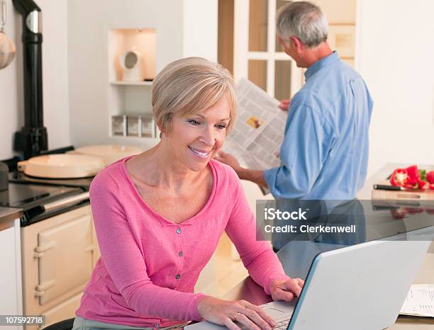 Mujer Madura Trabajando En La Computadora Portátil Con El Hombre Mayor En El Fondo Foto de stock y más banco de imágenes de Internet