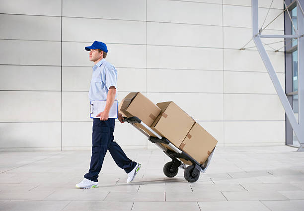 consegna uomo spinge il carrello di pacchetti in ufficio hall - hand truck foto e immagini stock