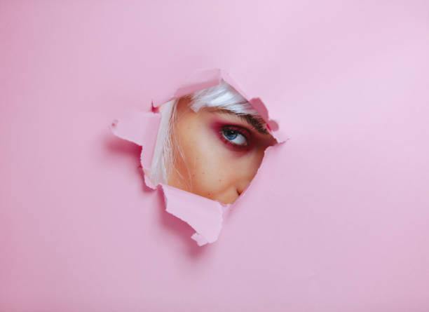 istock Female with eye makeup peeking through torn paper 1075975100