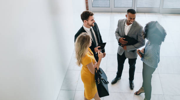 Corporate professionals having casual meeting in office lobby Group of young business professionals standing together and having casual discussing in office hallway. Business colleagues having casual meeting in office lobby. business lifestyle stock pictures, royalty-free photos & images
