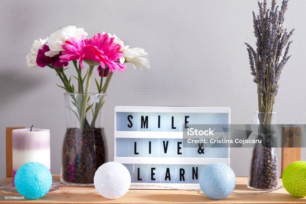 Flowers and home decorations set up with inspirational message 7 Lavander and colorful flowers in vase filled with coffee, candle and smile live and learn inspirational message written on light board Lightbox Stock Photo
