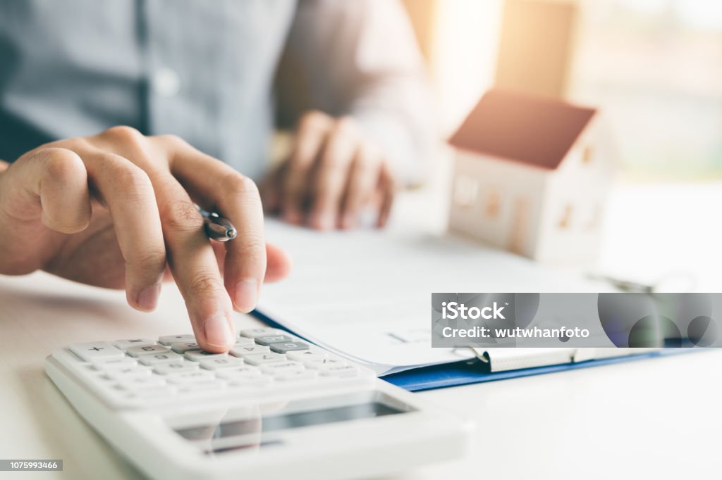 Home agents are using a calculator to calculate the loan period each month for the customer. Real Estate Stock Photo