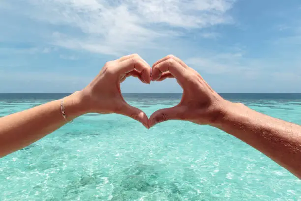 Photo of heart shape with a male and female hand. Clear blue water as background. Freedom in paradise concept