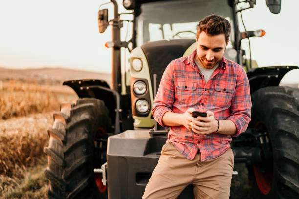 Modern agriculture with technology and machinery concept Portrait of smiling farmer using smartphone and tractor at harvesting. Modern agriculture with technology and machinery concept Farmer stock pictures, royalty-free photos & images