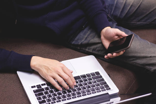 istock Closeup of man relaxing  using smartphone and laptop computer sitting on sofa. 1076033904