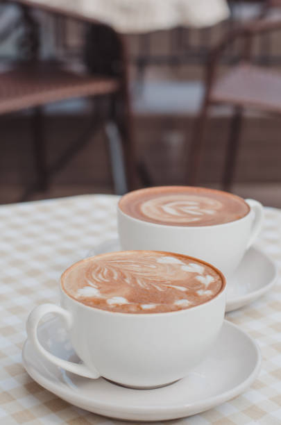A two cup of cappuccino or latte with a pattern on the table with a checkered tablecloth. The table is located on the terrace of a cozy cafe.