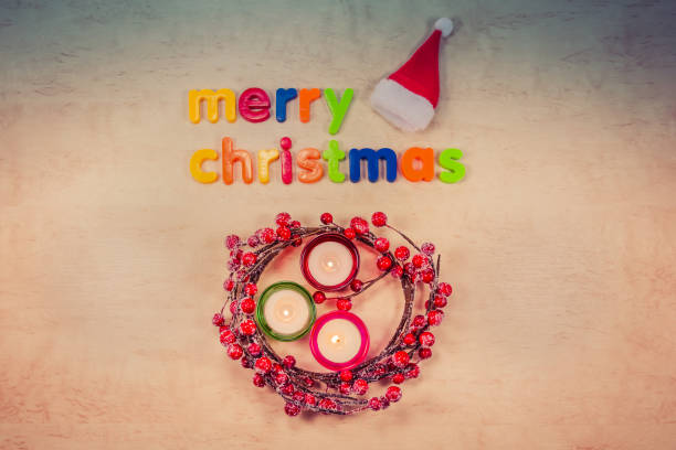 Merry Christmas concept - text on background, burning candles, wreath with berries and Santa Claus hat
