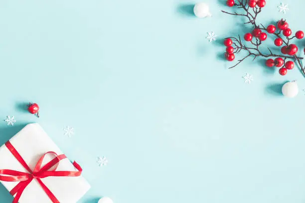 Photo of Christmas or winter composition. Gift, snowflakes, white balls and red berries on pastel blue background. Christmas, winter, new year concept. Flat lay, top view, copy space