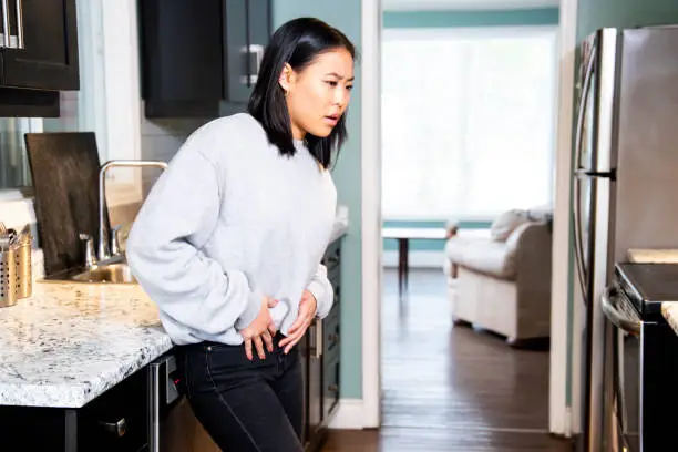 Photo of A young woman experiencing pelvic discomfort, she is grimacing in pain.