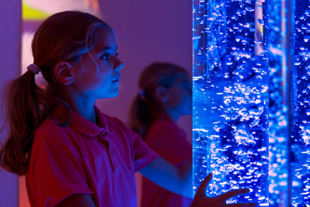 istock Child in therapy sensory stimulating room, snoezelen. Child interacting with colored lights bubble tube lamp during therapy session. 1076076128