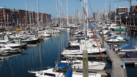 Scene Of Packed Land Vehicle, People, Office And Residential Building Exterior And Lots Of Docked Yachts At Scheveningen Marina In South Holland The Netherlands Europe