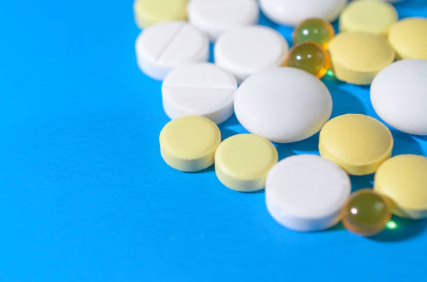 white and yellow pills on blue background close up. - straggling imagens e fotografias de stock