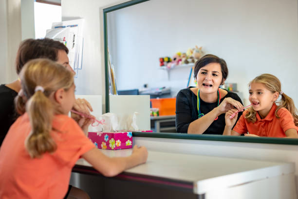 junge mädchen in logopädie büro. spiegelbild des jungen mädchens, die korrekte aussprache mit logopädin auszuüben. - child speech therapy adult stock-fotos und bilder