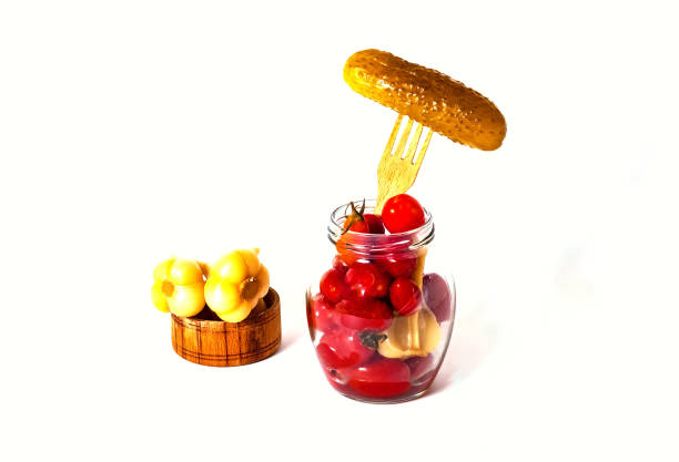 Pickled little tomatoes with garlic in glass jar and canned cucumber on wooden fork. Fermented food. Closeup. Copy space.