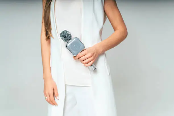 Photo of Elegant female journalist conducting business interview or press conference, hand with microphone over the grey background.