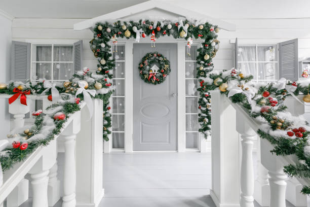 Christmas morning. house entrance decorated for holidays. Christmas decoration. garland of fir tree branches and lights on the railing Christmas morning. porch a small house with a decorated door with a Christmas wreath. Winter fairy tale wreath photos stock pictures, royalty-free photos & images