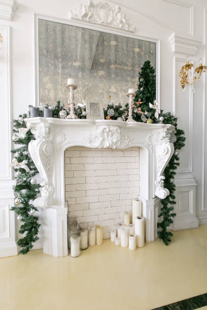 istock White fireplace decorated with candles and fir branches. Decorated Christmas tree. Classic apartments, morning in hotel 1076187490