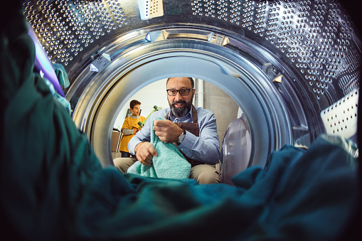 Photo of man doing laundry reaching inside washing machine