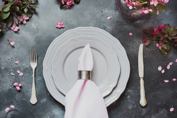 istock Spring elegant table place setting with romantic pink flowers, silverware on dark background. Top view. 1076195232