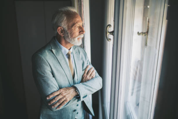 istock Senior man in suit standing by the window 1076196576