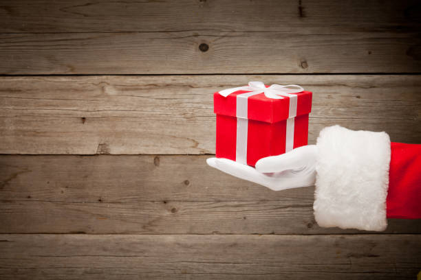 istock Santa hand holding a red gift box against wooden background 1076203414