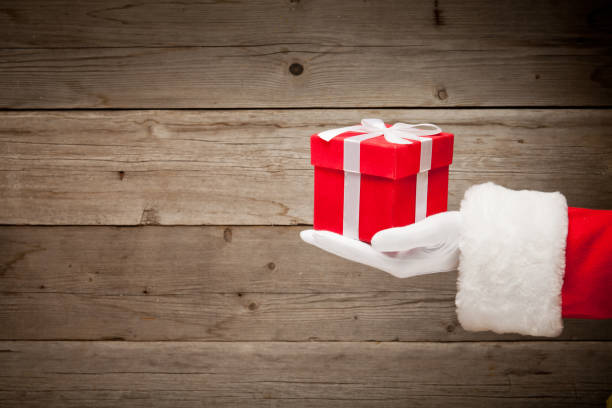 Santa hand holding a red gift box against wooden background stock photo
