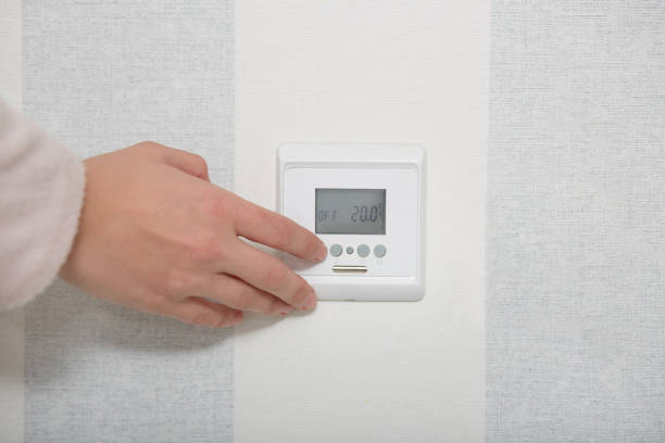 istock Smart home concept. Hands puches button switch on white wall, regulates temperature in flat or room. Close up, selective focus. Control panel 1076204628