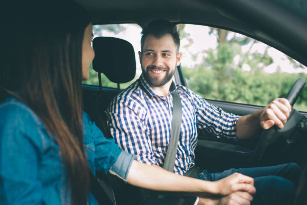 istock Careful driving. Beautiful young couple sitting on the front passenger seats and smiling while handsome man driving a car 1076211966
