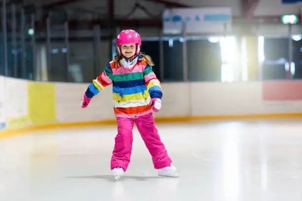 Child skating on indoor ice rink. Kids skate. Active family sport during winter vacation and cold season. Little girl in colorful wear training or learning ice skating. School sport activity and clubs