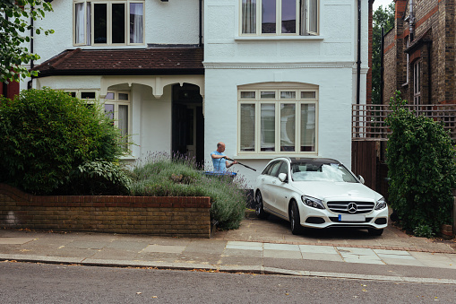 London/UK - July 21 2018: a man washing his white Mercedes on the terrace in front of his house in a suburb of London, UK