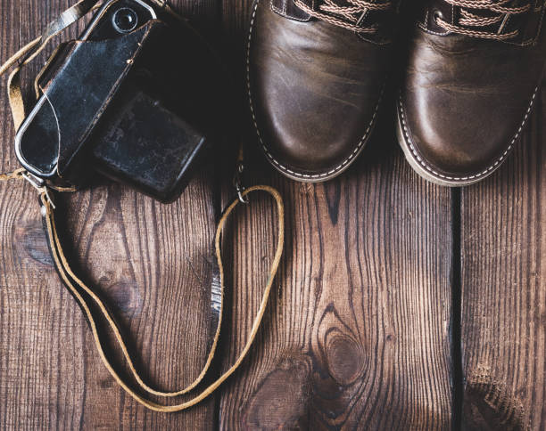 pair of leather brown shoes and an old vintage camera in a case on a wooden background, empty space
