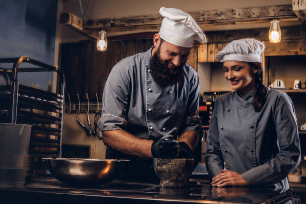 istock Chef grinds sesame seeds in a mortar for cooking bread. Chef teaching his assistant to bake the bread in bakery. 1076247688