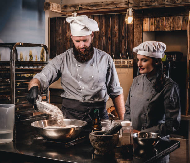 istock Chef pours the flour into a bowl. Chef teaching his assistant to bake the bread in the bakery. 1076248020