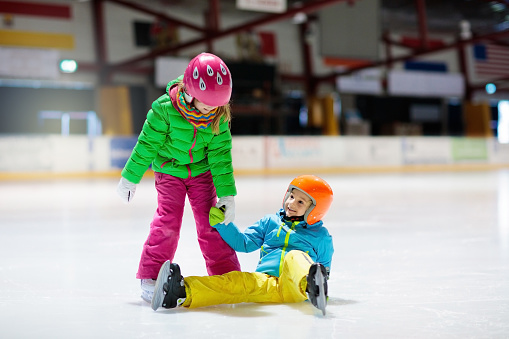 Child skating on indoor ice rink. Kids skate. Active family sport during winter vacation and cold season. Little girl and boy in colorful wear training or learning ice skating. School sport clubs