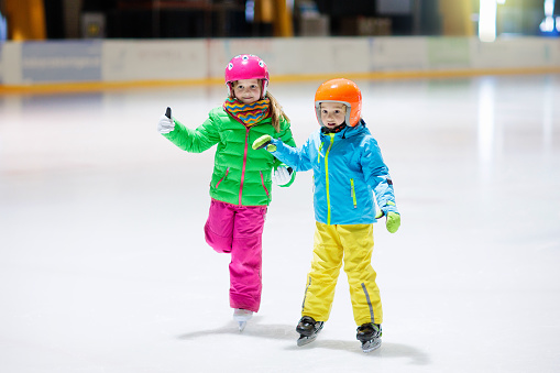 Child skating on indoor ice rink. Kids skate. Active family sport during winter vacation and cold season. Little girl and boy in colorful wear training or learning ice skating. School sport clubs