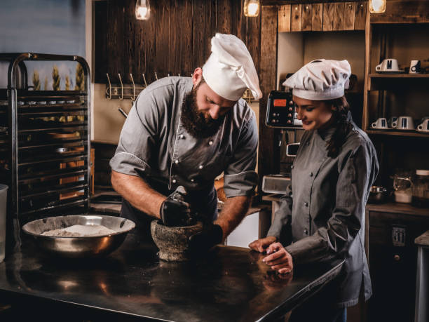 istock Chef grinds sesame seeds in a mortar for cooking bread. Chef teaching his assistant to bake the bread in bakery. 1076250070