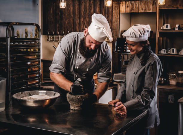 istock Chef grinds sesame seeds in a mortar for cooking bread. Chef teaching his assistant to bake the bread in bakery. 1076250396