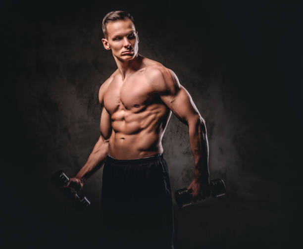 istock Young shirtless bodybuilder with muscular body doing exercise with dumbbells on dark background. 1076251228