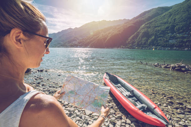 istock Female on lakeshore with red canoe looking at mountain map for directions 1076267544