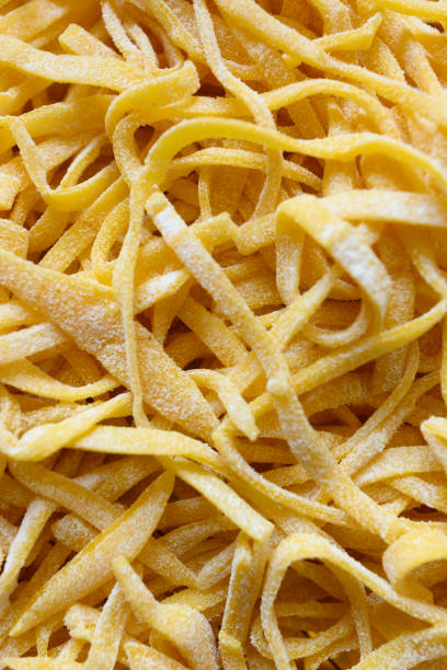 Fresh pasta called 'Fettuccine' made from fresh eggs and durum wheat flour. (selective focus) Fresh pasta called 'Fettuccine' made from fresh eggs and durum wheat flour. Fettuccine is a flat thick pasta popular in Roman and Tuscan cuisine. cooked selective focus vertical pasta stock pictures, royalty-free photos & images