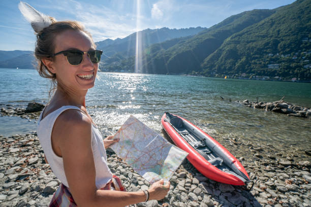 istock Female on lakeshore with red canoe looking at mountain map for directions 1076267792