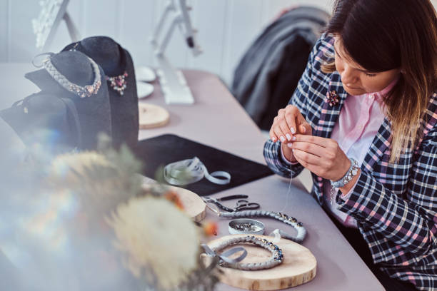 istock Elegantly dressed woman makes handmade necklaces, working with needles and thread in workshop. 1076282888