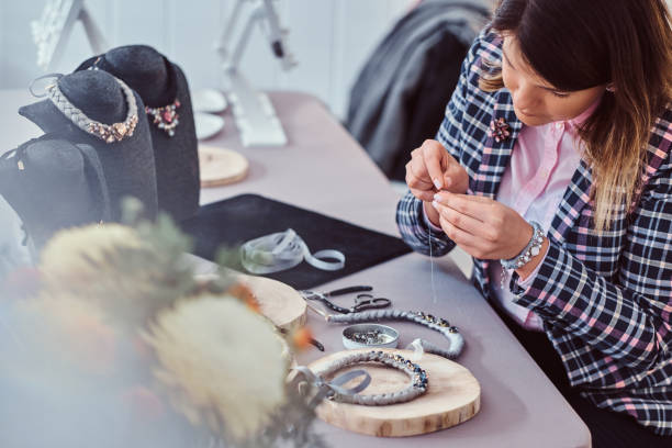 istock Elegantly dressed woman makes handmade necklaces, working with needles and thread in workshop. 1076283142