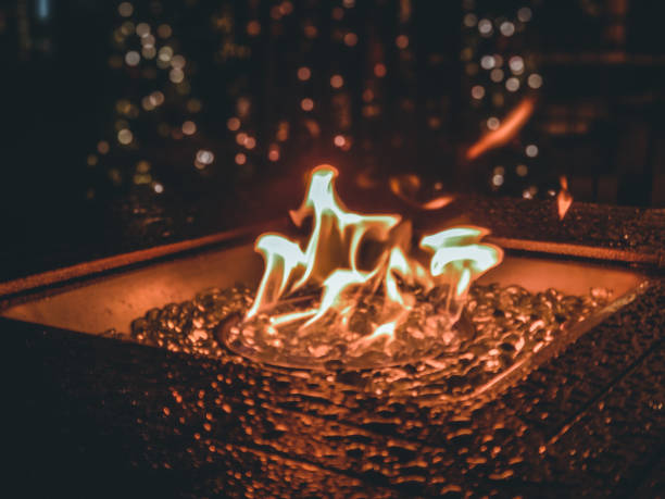 baile de llamas de gas en un fogón al aire libre con ladrillos de vidrio. decoración de árboles de navidad en el fondo con bokeh. - blue flame natural gas fireplace fotografías e imágenes de stock